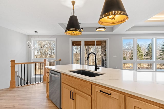 kitchen with decorative light fixtures, light stone counters, light wood-style flooring, stainless steel dishwasher, and a sink