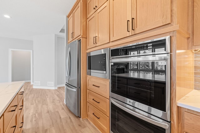 kitchen with baseboards, light stone countertops, light brown cabinetry, light wood-type flooring, and appliances with stainless steel finishes