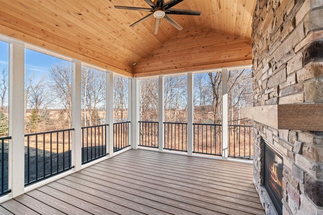 unfurnished sunroom with a wealth of natural light, an outdoor stone fireplace, wooden ceiling, ceiling fan, and vaulted ceiling