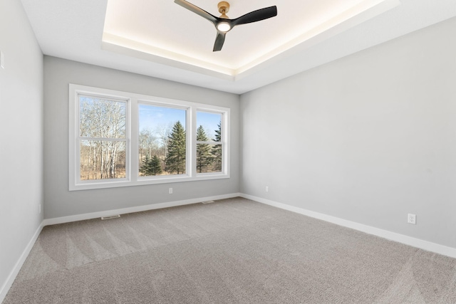 empty room with carpet flooring, baseboards, and a tray ceiling