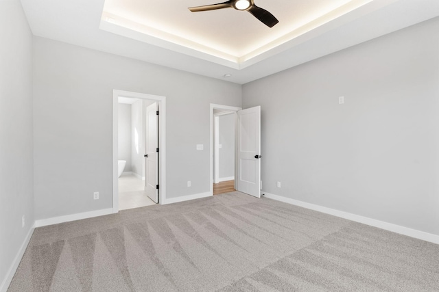 unfurnished bedroom with a tray ceiling, baseboards, carpet floors, and connected bathroom