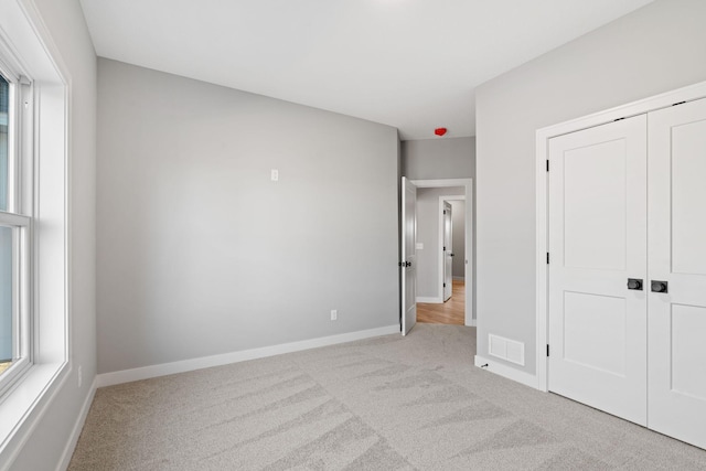 unfurnished bedroom with visible vents, baseboards, light colored carpet, and a closet