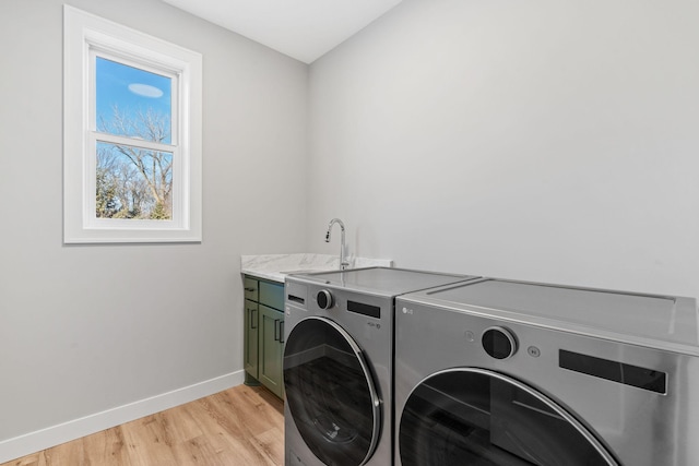 laundry area with baseboards, cabinet space, separate washer and dryer, a sink, and light wood-type flooring