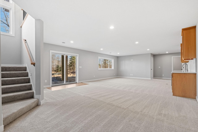 unfurnished living room featuring recessed lighting, light colored carpet, stairs, and baseboards