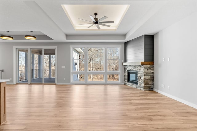 unfurnished living room with a wealth of natural light, a fireplace, a raised ceiling, and light wood-style floors