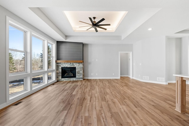 unfurnished living room with light wood-type flooring, visible vents, a tray ceiling, a fireplace, and baseboards