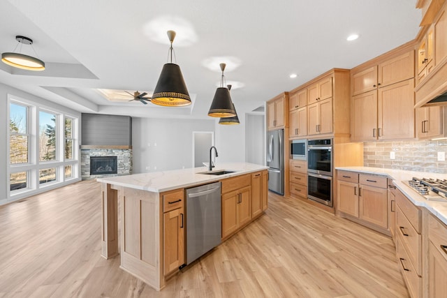 kitchen featuring backsplash, light brown cabinets, open floor plan, appliances with stainless steel finishes, and a sink