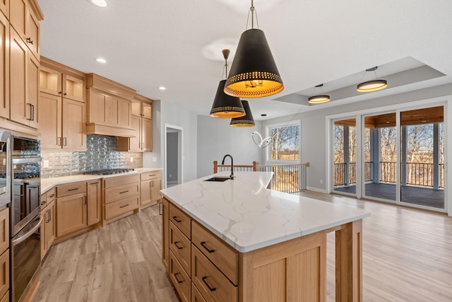 kitchen with backsplash, an island with sink, appliances with stainless steel finishes, a raised ceiling, and a sink