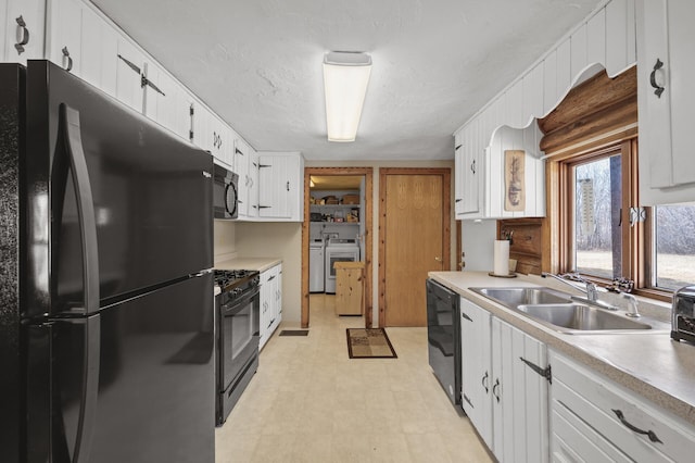 kitchen featuring washer and clothes dryer, light floors, white cabinets, black appliances, and a sink