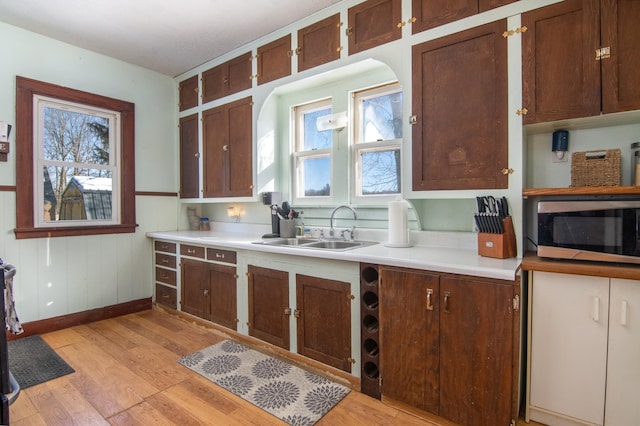 kitchen with a sink, stainless steel microwave, light countertops, and light wood finished floors