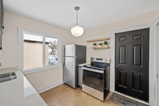 kitchen featuring baseboards, pendant lighting, appliances with stainless steel finishes, light wood-style floors, and a sink