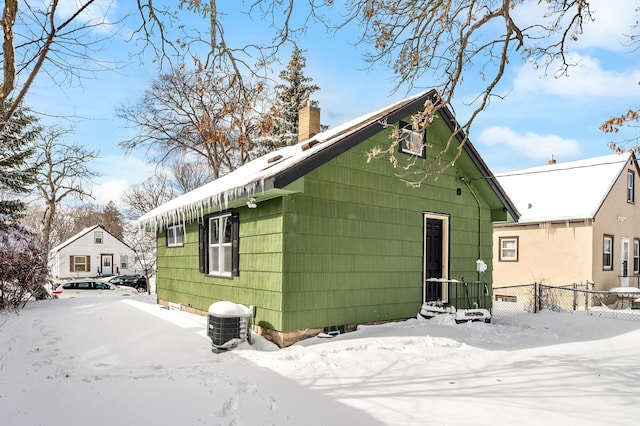 snow covered back of property with central air condition unit, a chimney, and fence