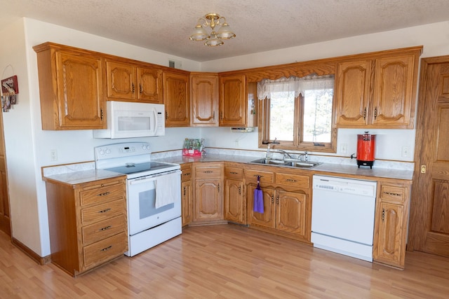 kitchen featuring white appliances, brown cabinetry, light wood finished floors, a sink, and a chandelier