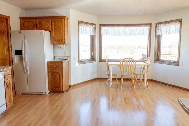 kitchen featuring baseboards, light countertops, light wood-style flooring, brown cabinets, and white appliances