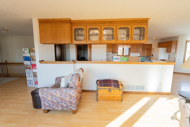 kitchen with visible vents, brown cabinets, white fridge with ice dispenser, and light wood-style flooring