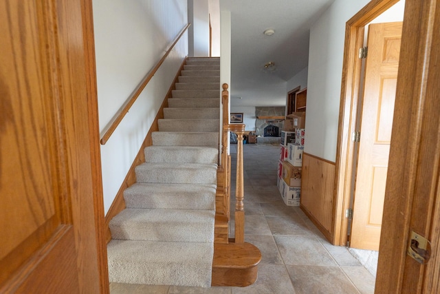 stairs with a wainscoted wall, a fireplace, and wooden walls