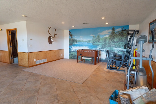 rec room with a wainscoted wall, visible vents, a textured ceiling, wooden walls, and tile patterned flooring