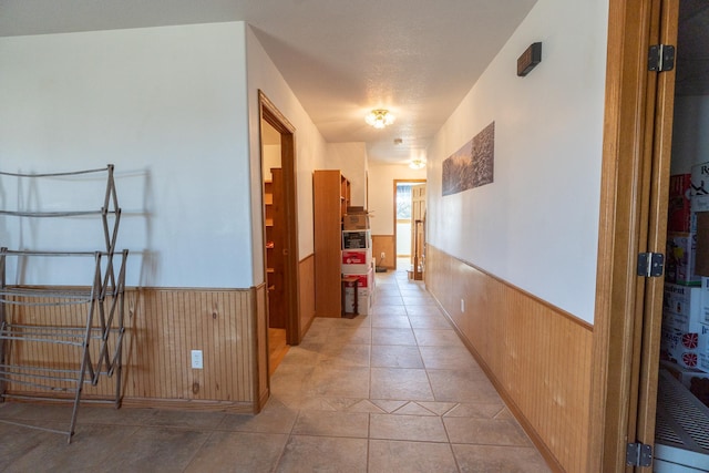 hall featuring light tile patterned floors, a wainscoted wall, and wooden walls