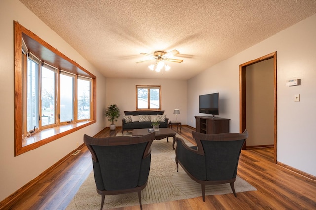 living area featuring a textured ceiling, wood finished floors, baseboards, and ceiling fan