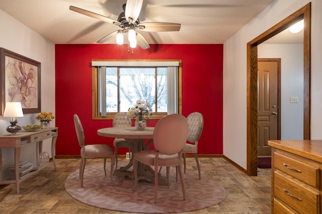 dining room featuring a textured ceiling, a ceiling fan, stone finish flooring, and baseboards