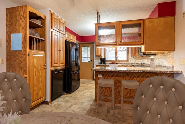 kitchen with a breakfast bar, a peninsula, freestanding refrigerator, glass insert cabinets, and a textured ceiling