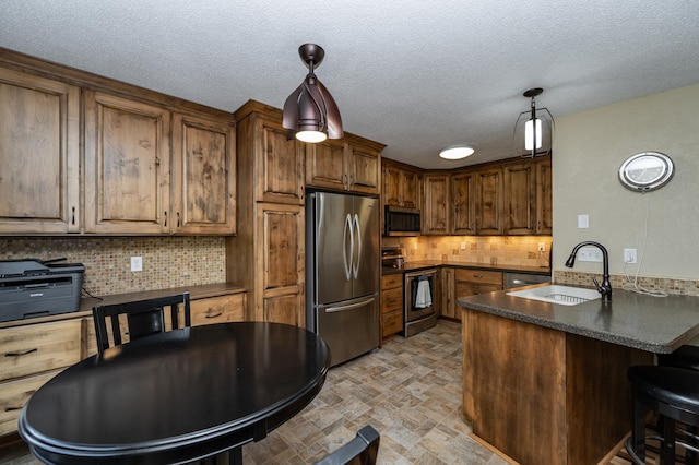 kitchen featuring dark countertops, tasteful backsplash, a peninsula, stainless steel appliances, and a sink