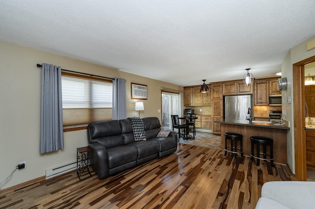 living area featuring a baseboard radiator, a textured ceiling, and wood finished floors