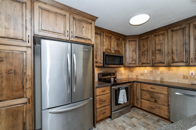 kitchen featuring dark stone countertops, decorative backsplash, stone finish floor, appliances with stainless steel finishes, and a textured ceiling