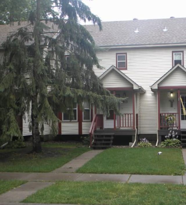 view of property featuring covered porch, a shingled roof, and a front yard