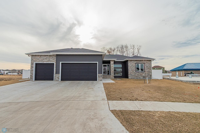 prairie-style home featuring stone siding, an attached garage, driveway, and a front lawn