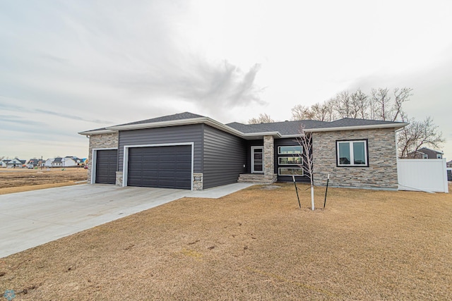 view of front of home featuring a front yard, a shingled roof, concrete driveway, a garage, and stone siding