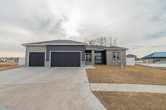 prairie-style house featuring a front lawn, an attached garage, stone siding, and driveway