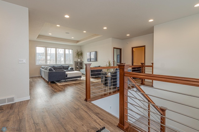 corridor featuring hardwood / wood-style floors, visible vents, recessed lighting, a raised ceiling, and an upstairs landing