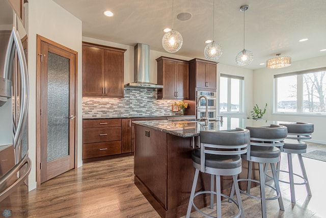 kitchen featuring tasteful backsplash, appliances with stainless steel finishes, wall chimney exhaust hood, and a kitchen breakfast bar