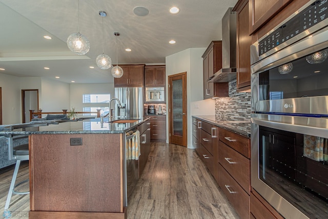 kitchen featuring a breakfast bar area, dark wood-type flooring, appliances with stainless steel finishes, wall chimney exhaust hood, and backsplash