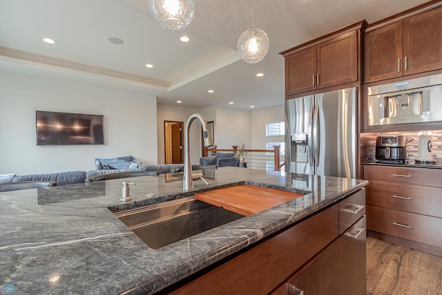 kitchen with dark stone counters, a sink, stainless steel refrigerator with ice dispenser, a raised ceiling, and open floor plan