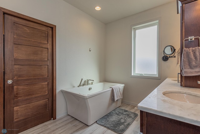 full bath featuring wood finished floors, baseboards, a soaking tub, double vanity, and a sink