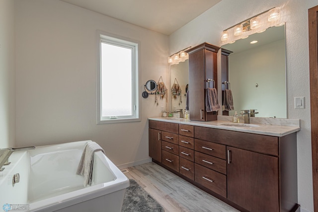 full bathroom with double vanity, a soaking tub, wood finished floors, and a sink