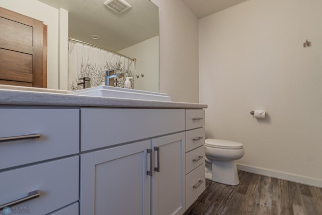 bathroom with vanity, wood finished floors, visible vents, baseboards, and toilet