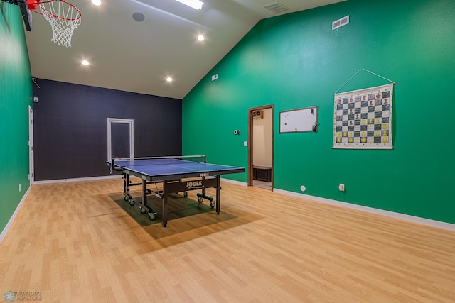 recreation room featuring wood finished floors, visible vents, baseboards, high vaulted ceiling, and an accent wall