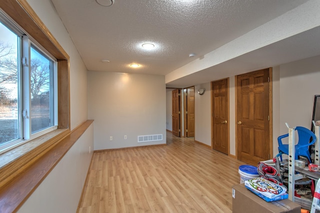 playroom featuring baseboards, visible vents, a textured ceiling, and light wood-style floors