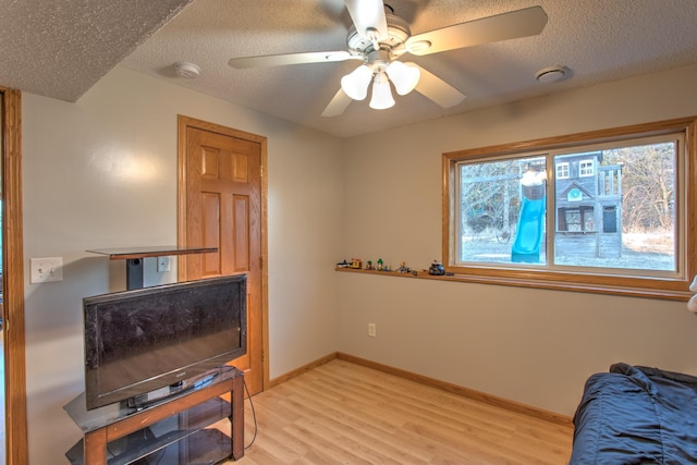 interior space with baseboards, a textured ceiling, ceiling fan, and light wood finished floors