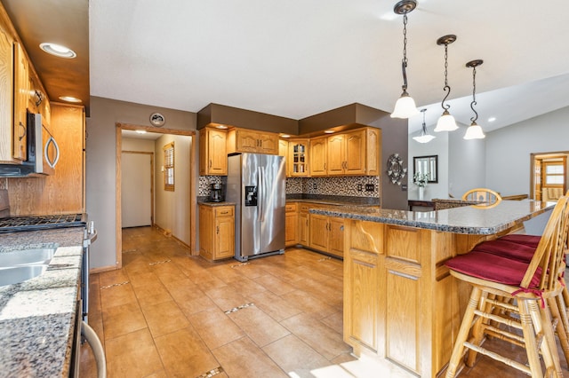 kitchen with tasteful backsplash, glass insert cabinets, brown cabinets, a kitchen breakfast bar, and stainless steel appliances