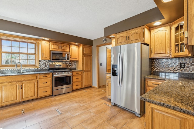 kitchen featuring backsplash, appliances with stainless steel finishes, glass insert cabinets, and a sink