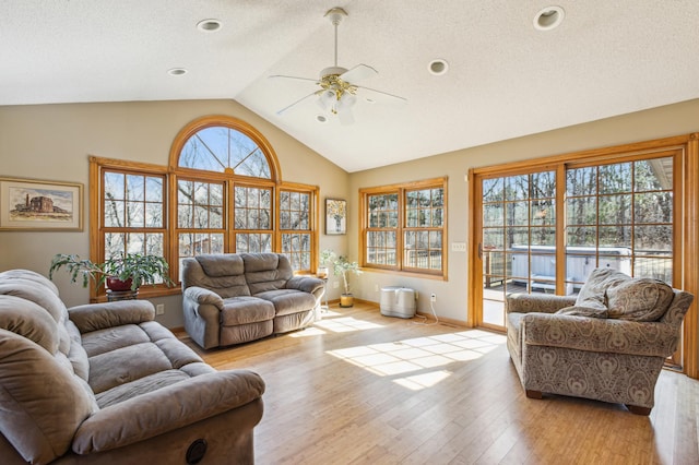 living area with lofted ceiling, a ceiling fan, light wood-style floors, and a wealth of natural light