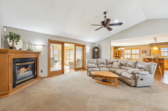 carpeted living area featuring ceiling fan with notable chandelier, a fireplace, and vaulted ceiling