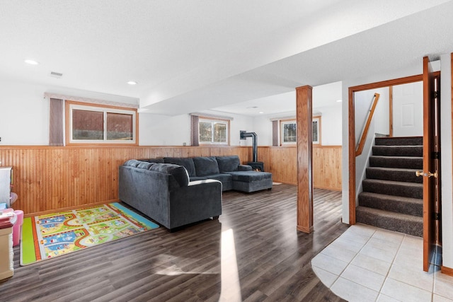 living area featuring visible vents, a wainscoted wall, wood walls, stairs, and a wood stove