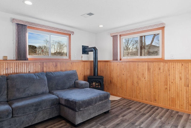 living area featuring a wainscoted wall, a wood stove, a healthy amount of sunlight, and visible vents