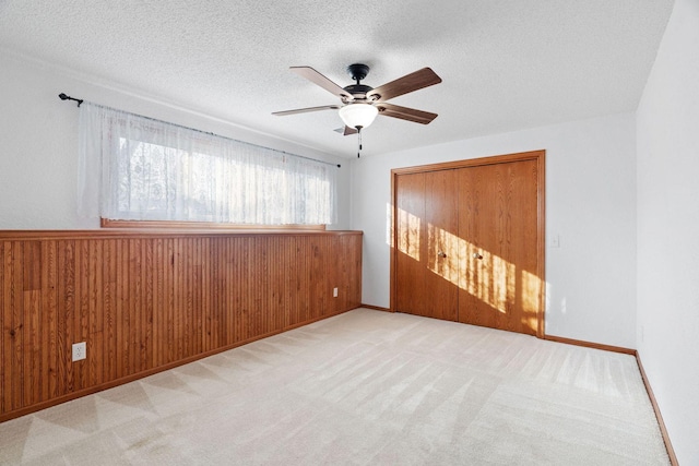 unfurnished bedroom with wooden walls, baseboards, ceiling fan, a textured ceiling, and carpet flooring