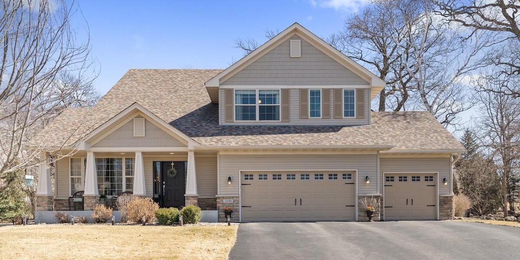 craftsman house with a shingled roof, covered porch, stone siding, and aphalt driveway